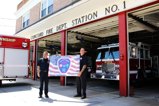 Two Concord Township firefighters hold department flag in front of fire station 